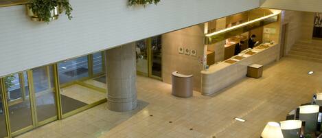 A modern hotel lobby with a reception desk, seating area, and decorative plants.