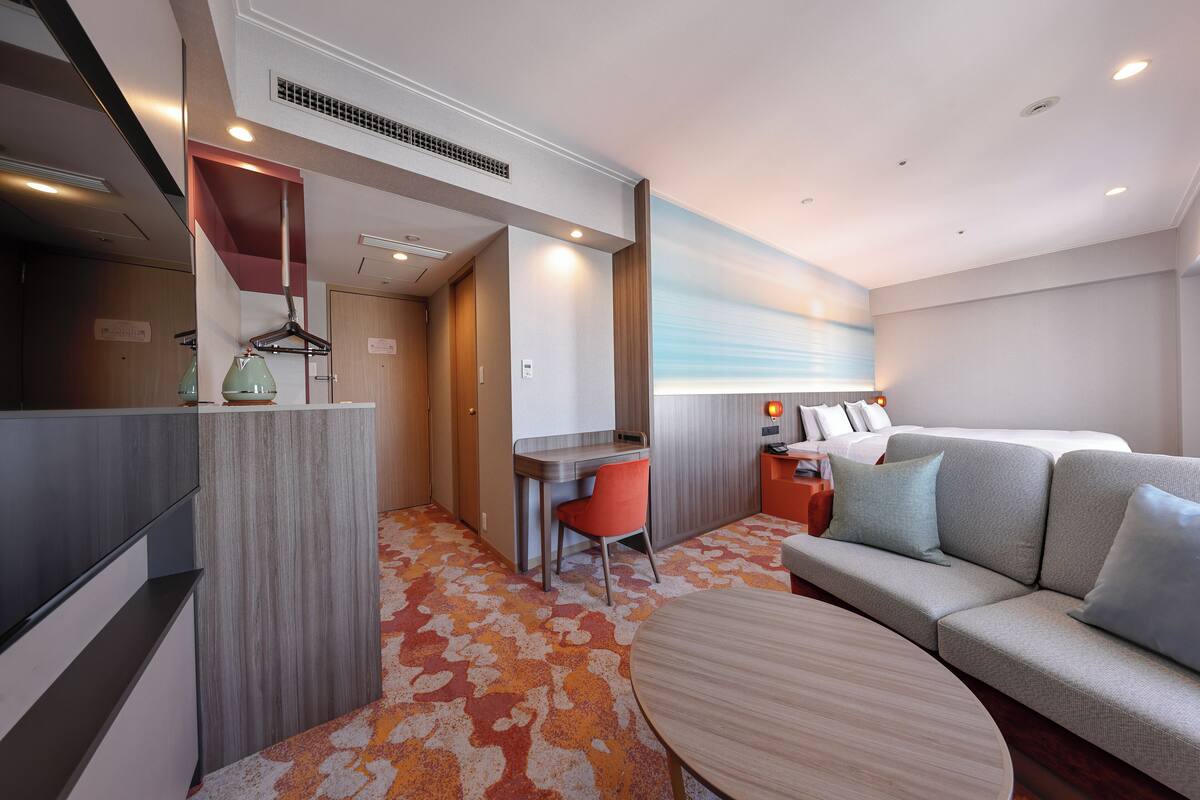 Een moderne hotelkamer met een bank, bureau, stoel, bed en een groot raam.