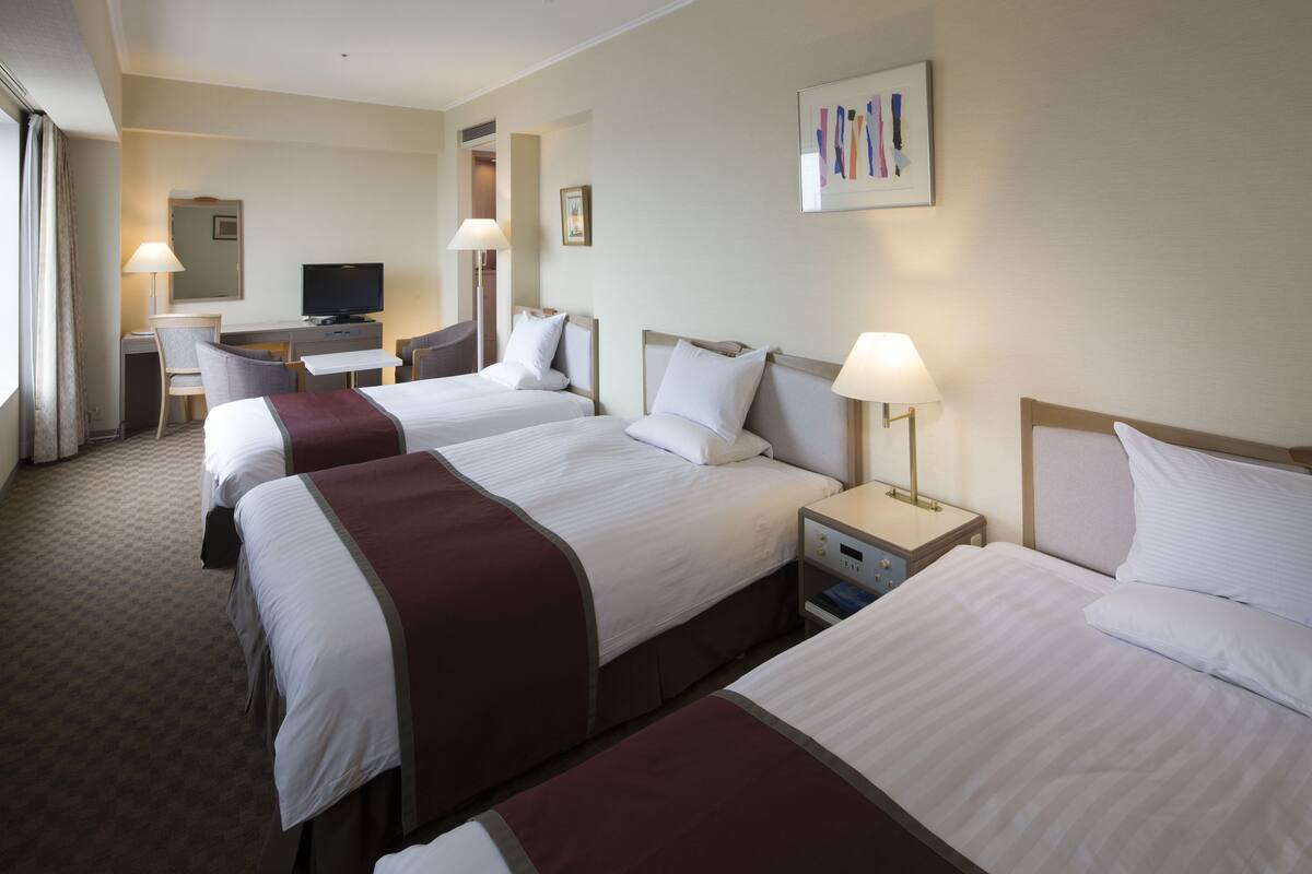 Een hotelkamer met drie bedden, een bureau met een televisie en een stoel.