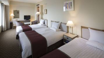 A hotel room with three beds, a desk with a television, and a chair.