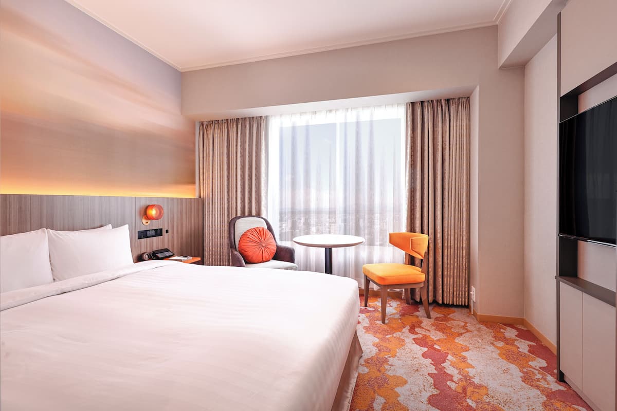 Een hotelkamer met een groot bed, een bureau met stoel, een tafeltje en een televisie.