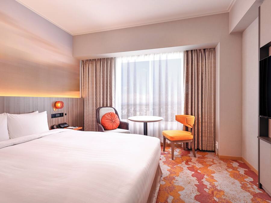 A hotel room with a large bed, a desk with a chair, a small table, and a TV.