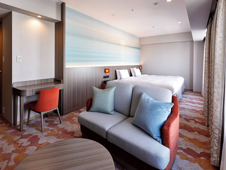 A hotel room with a bed, a sofa, a desk, and a chair.