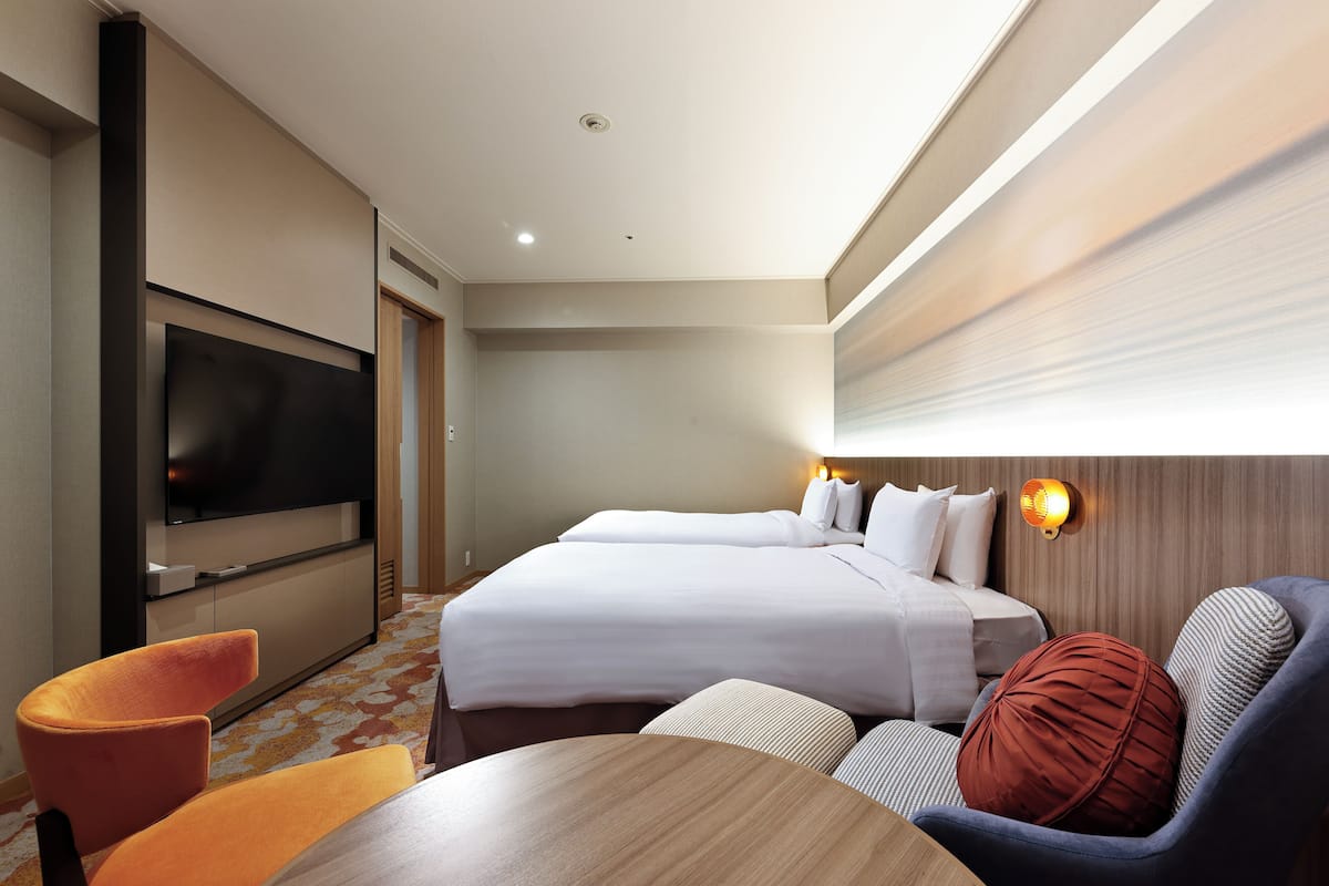 Een hotelkamer met twee bedden, een televisie, een houten tafel en een bank.