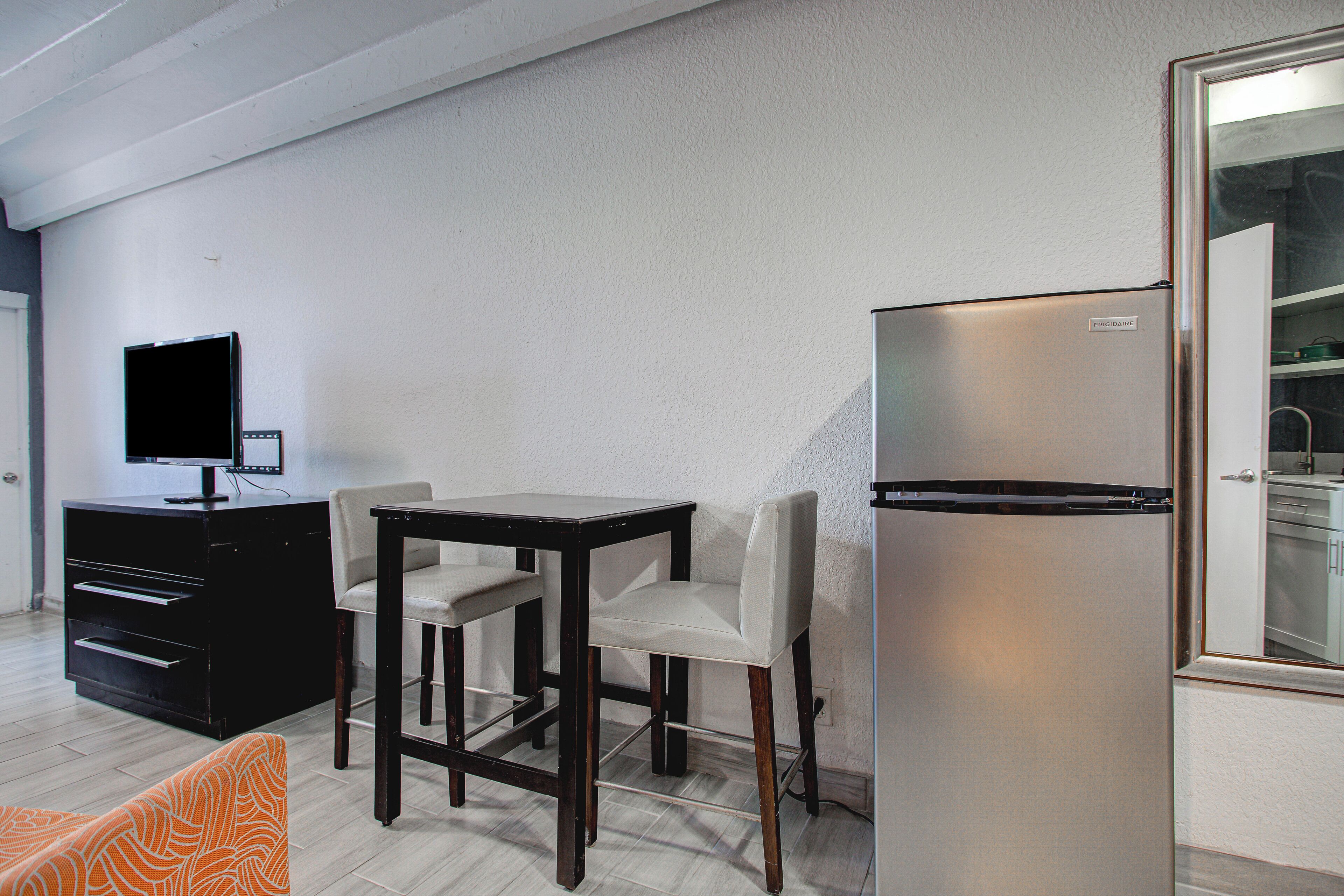 A compact living space with a dining table, chairs, a television, and a refrigerator.