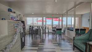 A spacious lobby with a check-in counter, seating area, and large windows with red umbrellas. - The Beach House Inn (Daytona Beach)