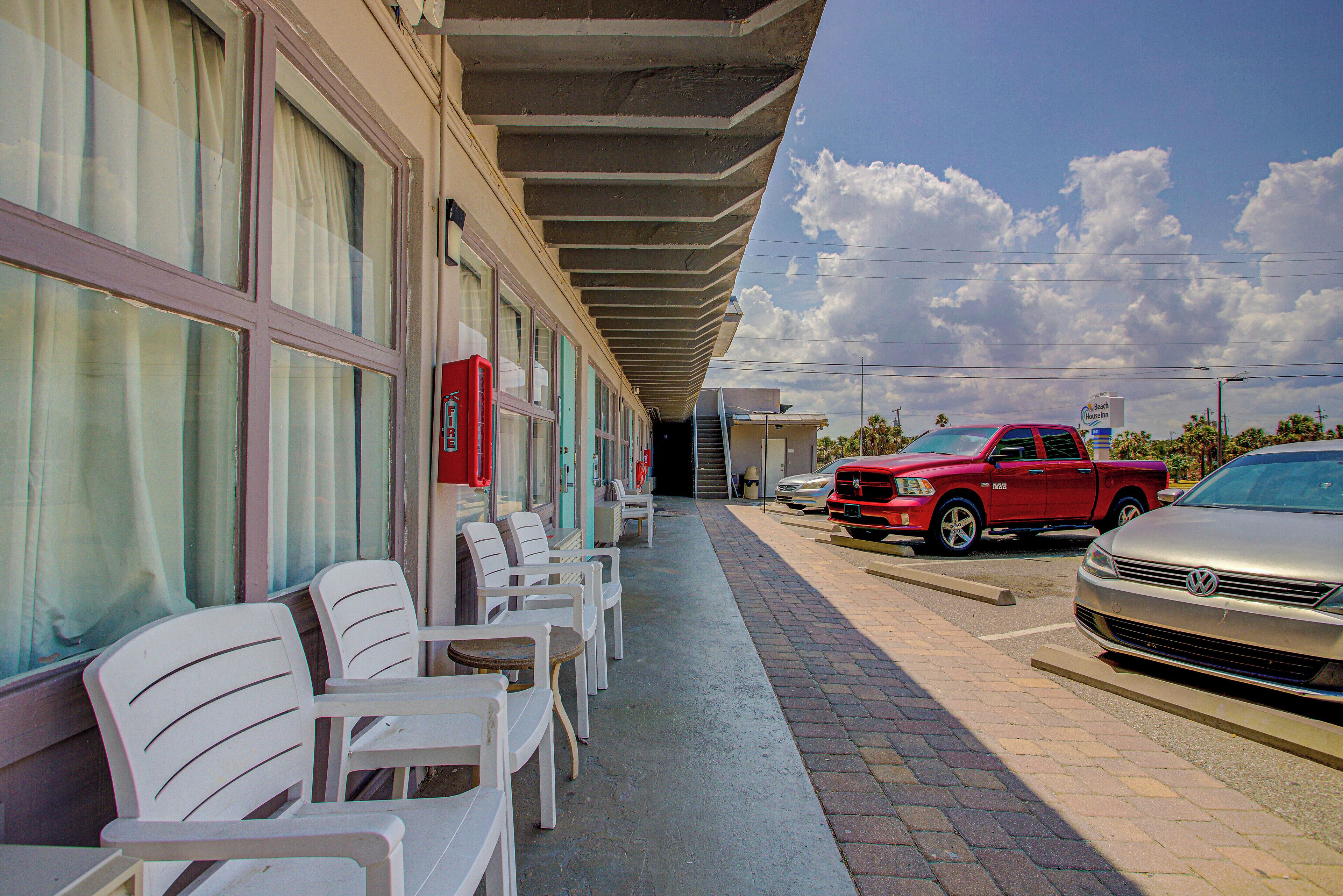 A hotel with a covered outdoor seating area, a fire alarm, and parked vehicles.