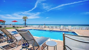 A pool area with lounge chairs and umbrellas, a clear sky, and a view of the ocean. - The Beach House Inn (Daytona Beach)