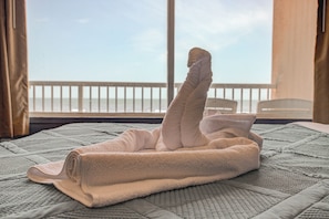 A neatly folded towel on a bed with a view of the sea through a balcony. - The Beach House Inn (Daytona Beach)
