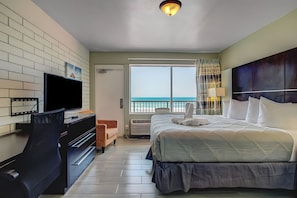 A hotel room with a bed, a desk, a chair, a TV, and a view of the ocean. - The Beach House Inn (Daytona Beach)