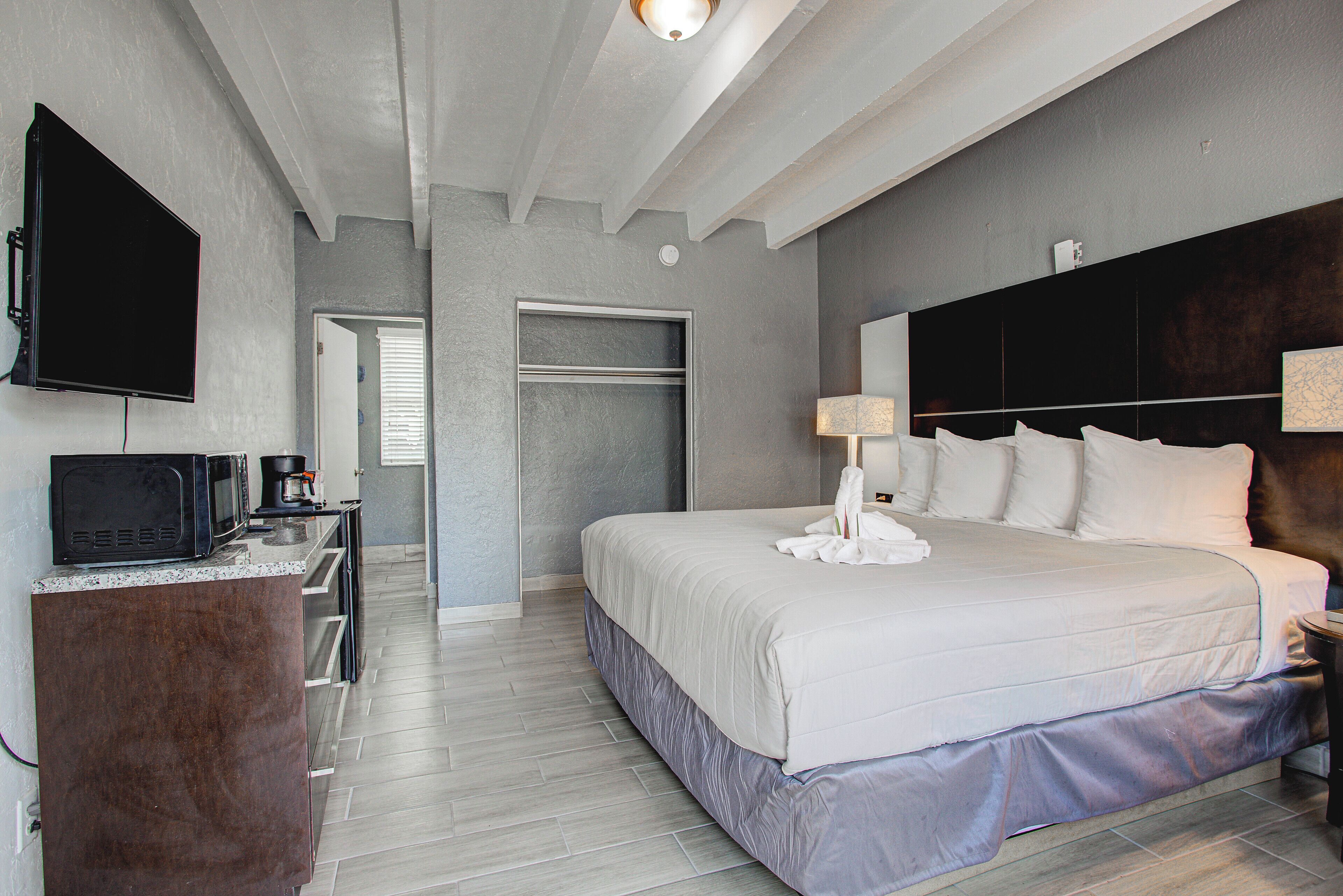 Una habitación de hotel con cama, escritorio con televisor, lámpara y armario.