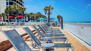 A beachside lounge with sun loungers and umbrellas, a pool, and a view of the ocean. - The Beach House Inn (Daytona Beach)