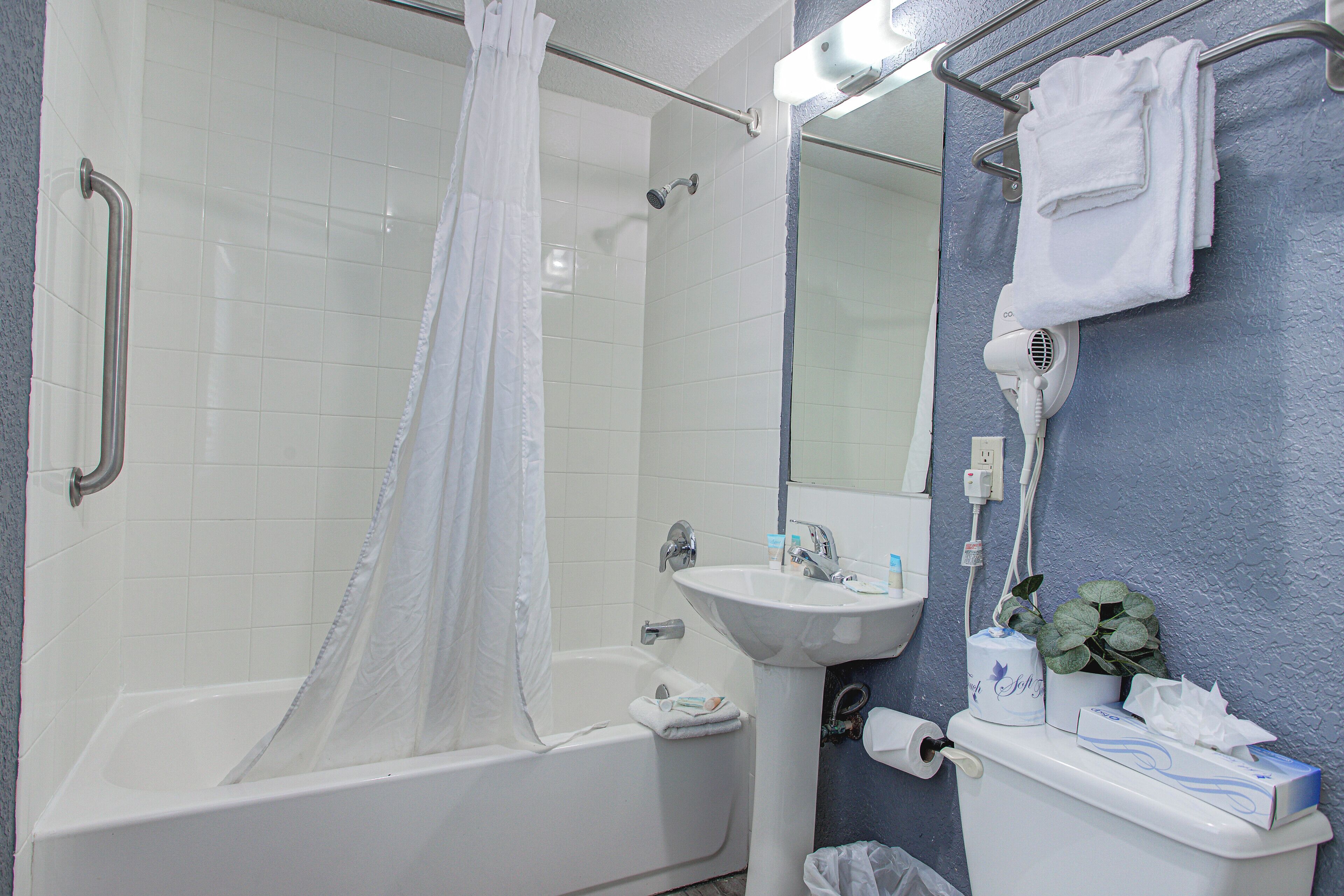 A bathroom with a bathtub, a shower curtain, a sink, a mirror, a towel rack, and a hairdryer.