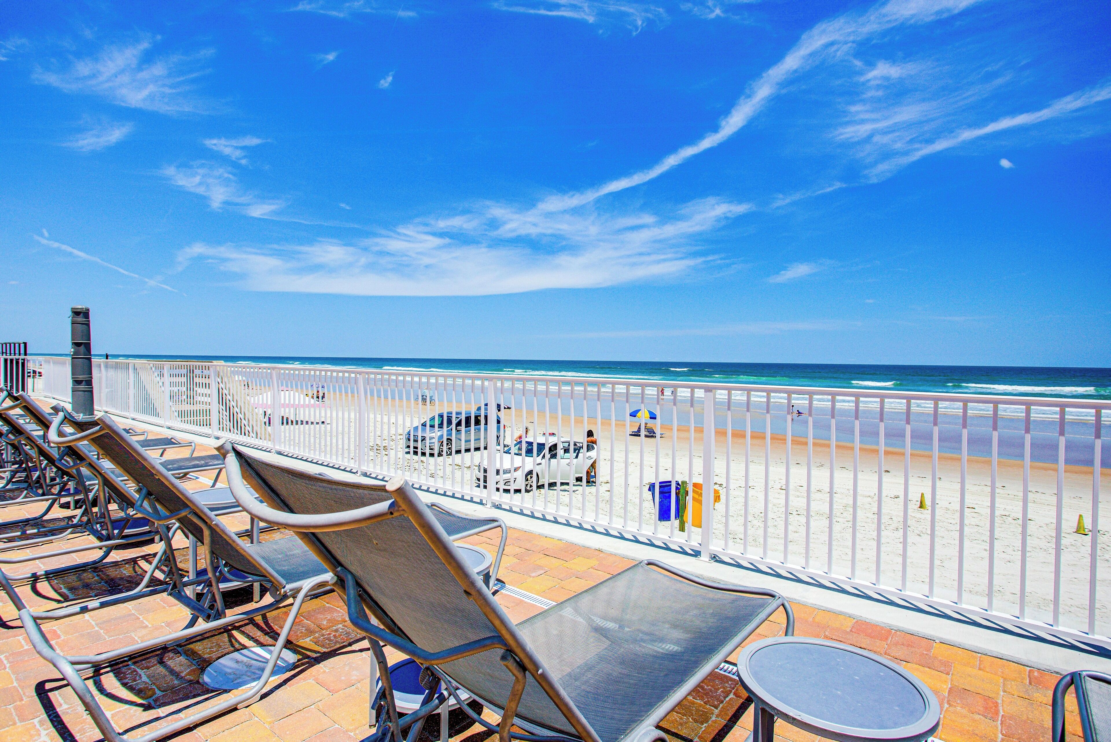 A beachside view with a railing, beach chairs, and a table.