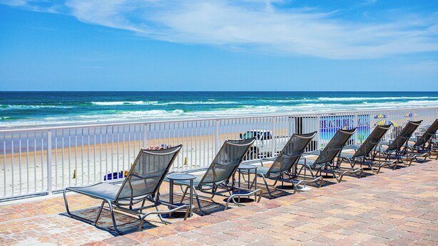 A beachside view with a row of sun loungers and a white fence. - The Beach House Inn (Daytona Beach)