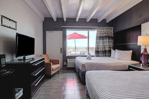 A hotel room with a television, a desk, a chair, two beds, a window with curtains, and a view of the sea. - The Beach House Inn (Daytona Beach)
