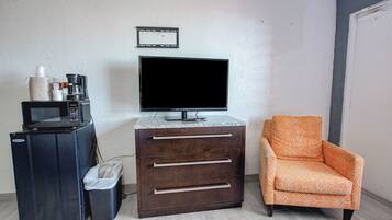 A room with a television, a coffee maker, a trash bin, a cabinet with drawers, and an orange patterned chair.