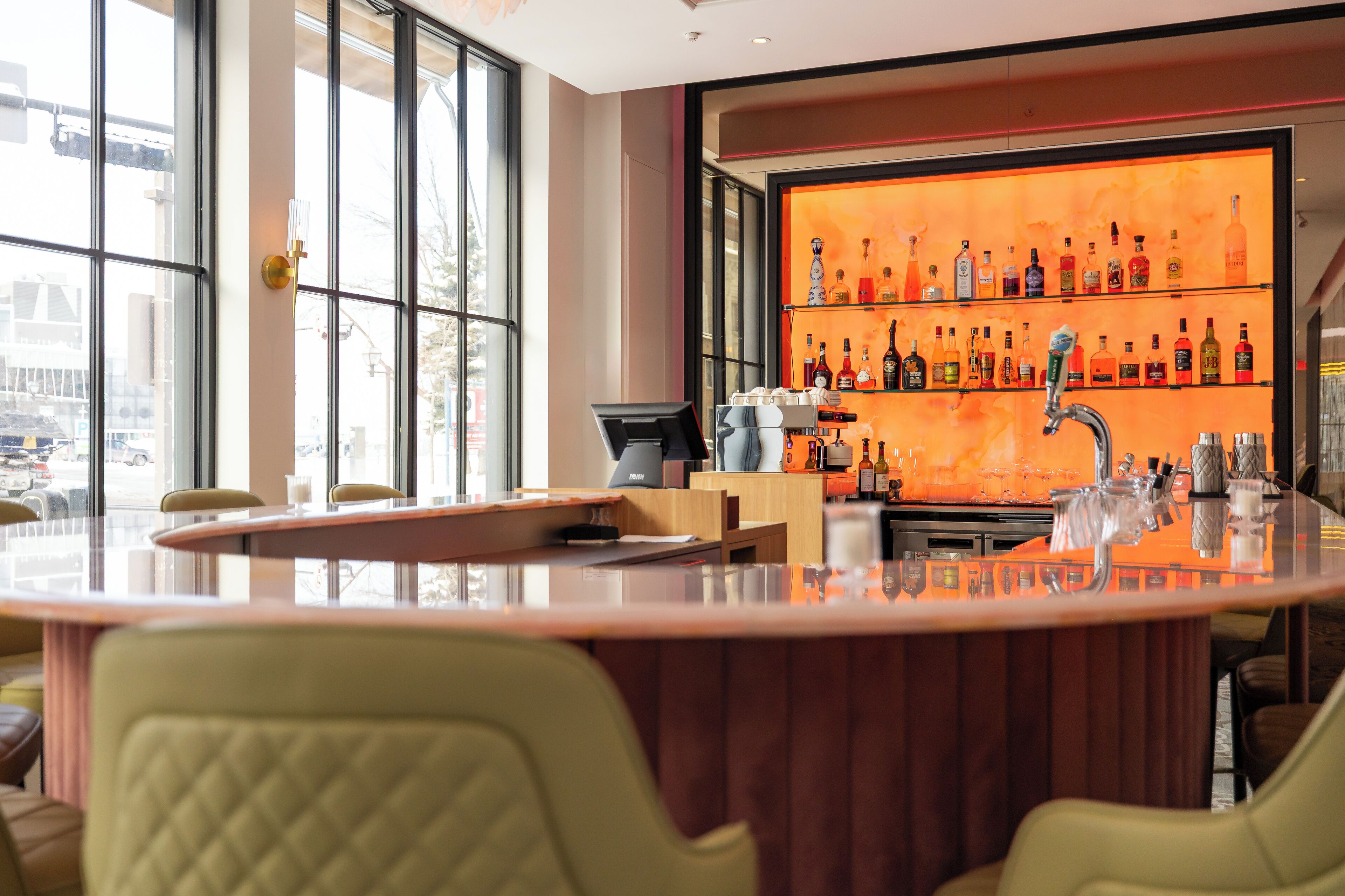 Eine Bar mit großem Fenster, einer Theke und einer Flaschenregal.