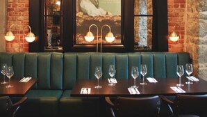 A restaurant interior with a brick wall, a framed poster of a woman, and a green booth seating area.