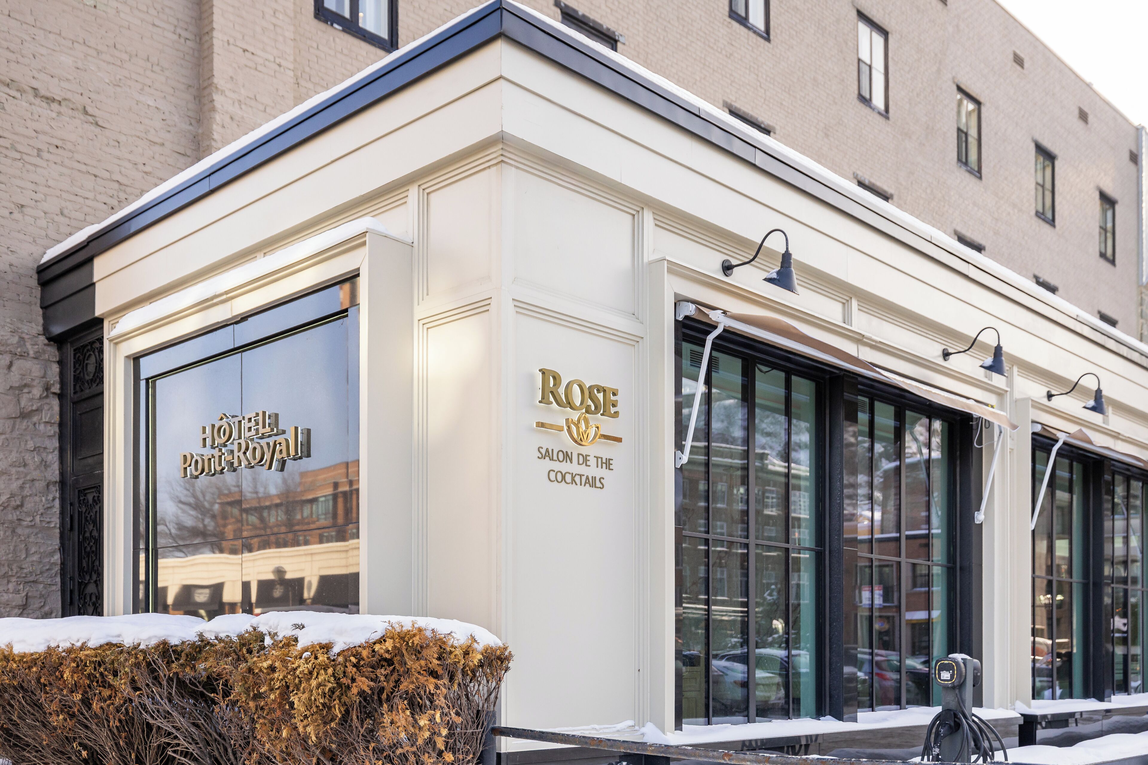 A hotel exterior with a large window, a sign reading "Rose Salon de la Cocktail," and a snow-covered ground.