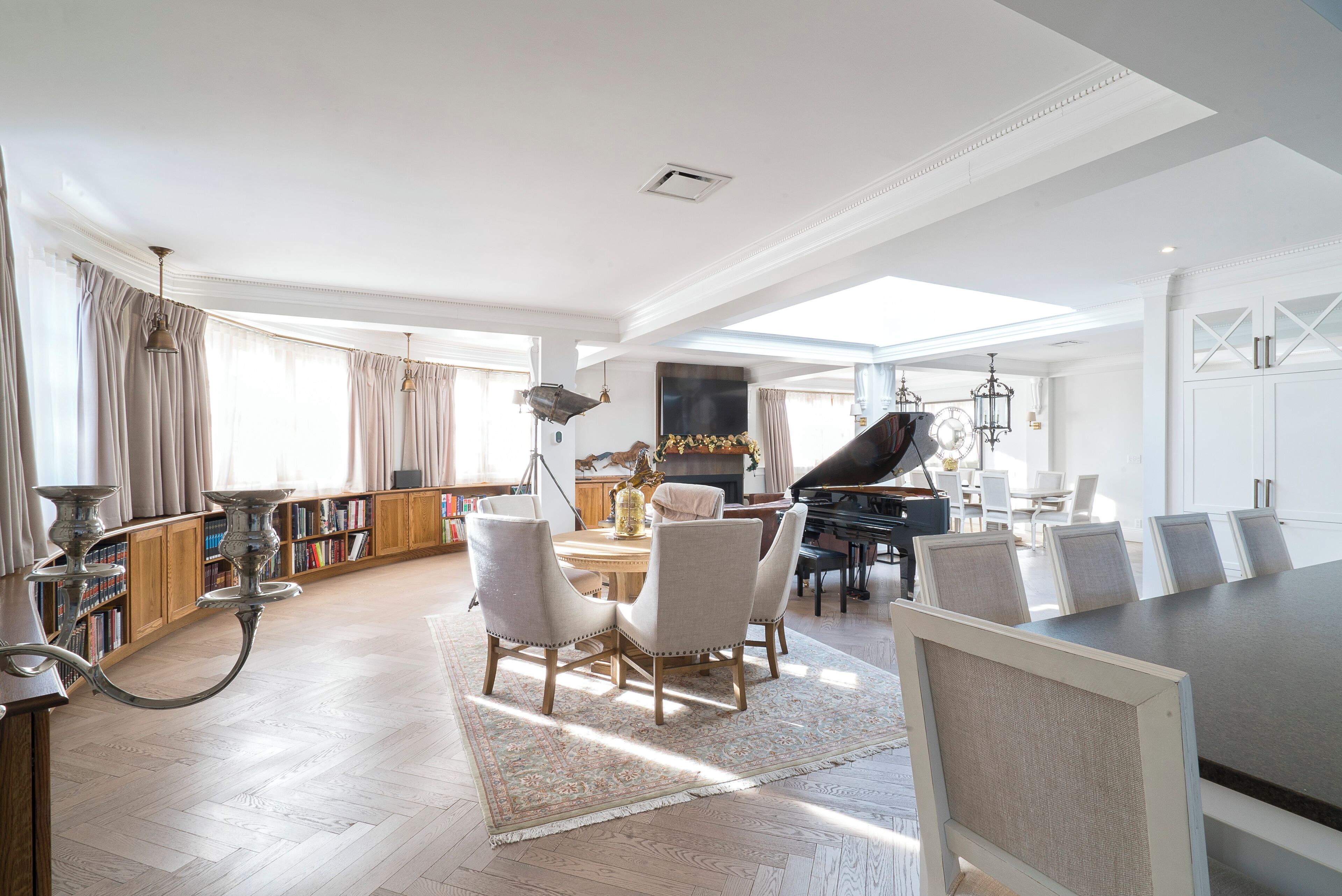 A spacious living room with a piano, a dining area, and a library.
