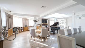 A spacious living room with a piano, a dining area, and a library.