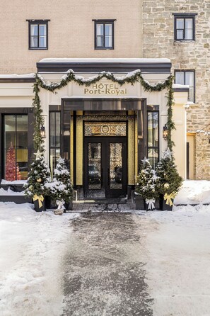 L’entrée d’un hôtel, avec un chemin enneigé, décoré de sapins de Noël et de guirlandes.