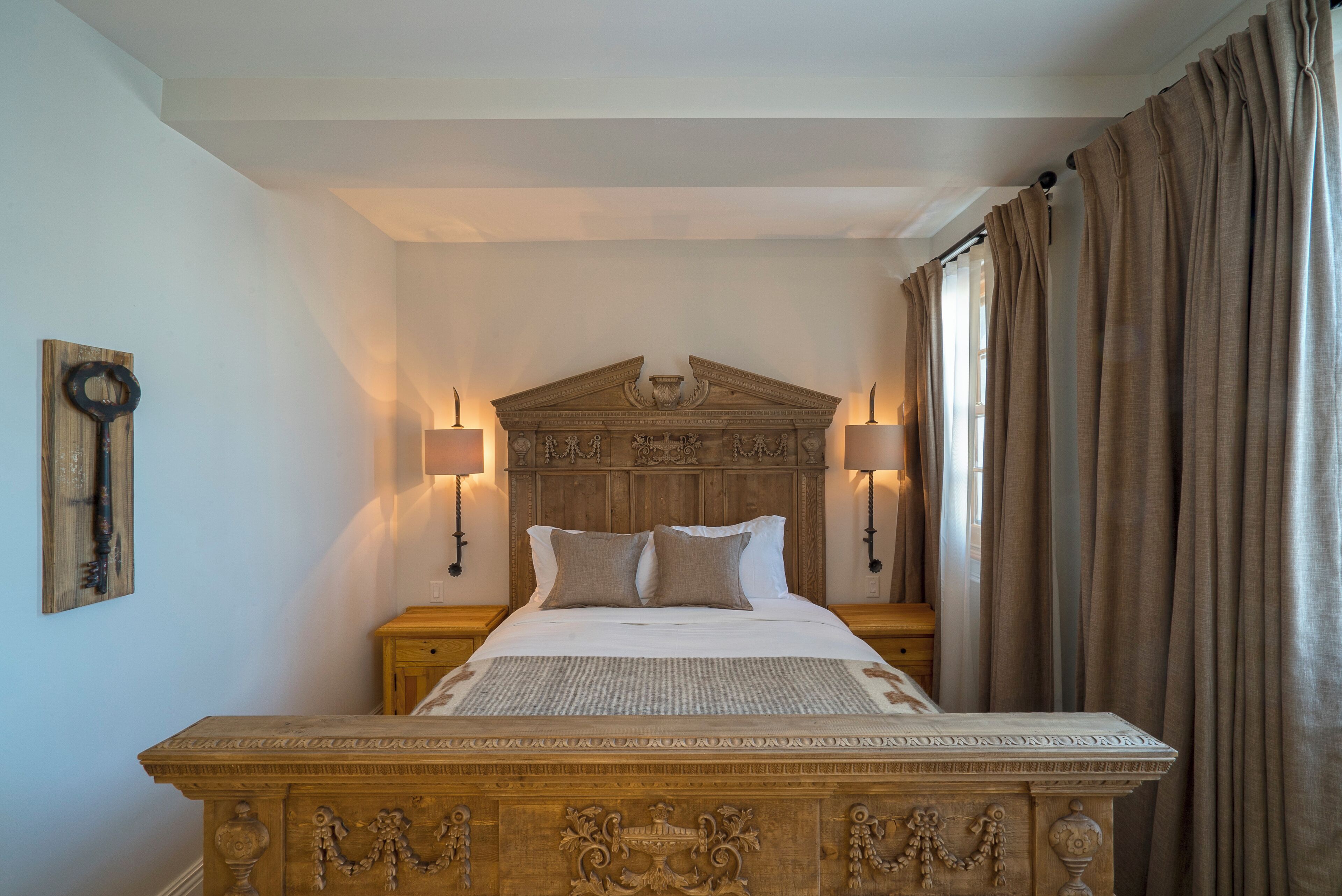 A bedroom with a wooden headboard, two bedside lamps, a bed with pillows, and a nightstand.