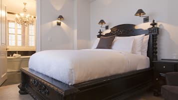 Una cama bien hecha con un cabecero de madera oscura, dos lámparas de noche y una araña en el fondo.