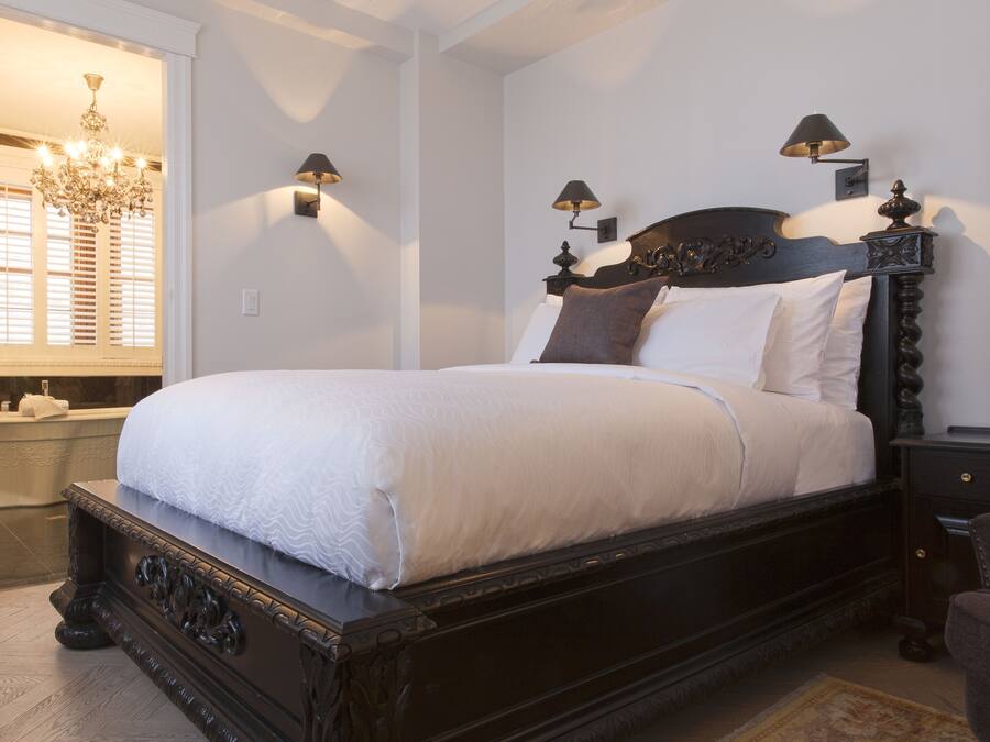 Una cama bien hecha con un cabecero de madera oscura, dos lámparas de noche y una araña en el fondo.