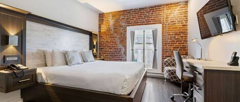 Un dormitorio moderno con pared de ladrillo, una cama grande, un escritorio y una silla.