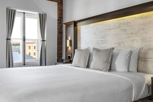 Una habitación de hotel moderna con una cama grande, un muro de ladrillo decorativo y vistas a la ciudad a través de la ventana.
