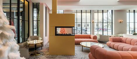 A modern lounge area with a fireplace, plush seating, and large windows offering city views.