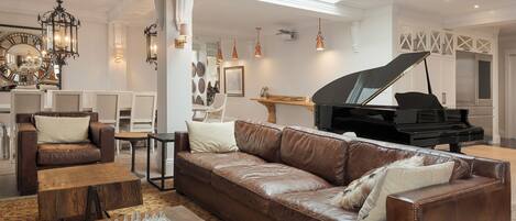 A spacious living room with a grand piano, leather sofas, a chessboard, and a chandelier.
