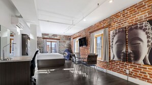A modern hotel room with a brick wall, a large Buddha painting, a bed, a desk, and a chair.
