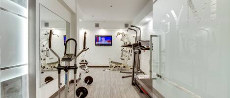 A modern gym with cardio equipment, weight machines, and a television screen.
