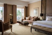 A hotel room with a large bed, a sofa, a chair, a coffee table, and a view of the outdoors.