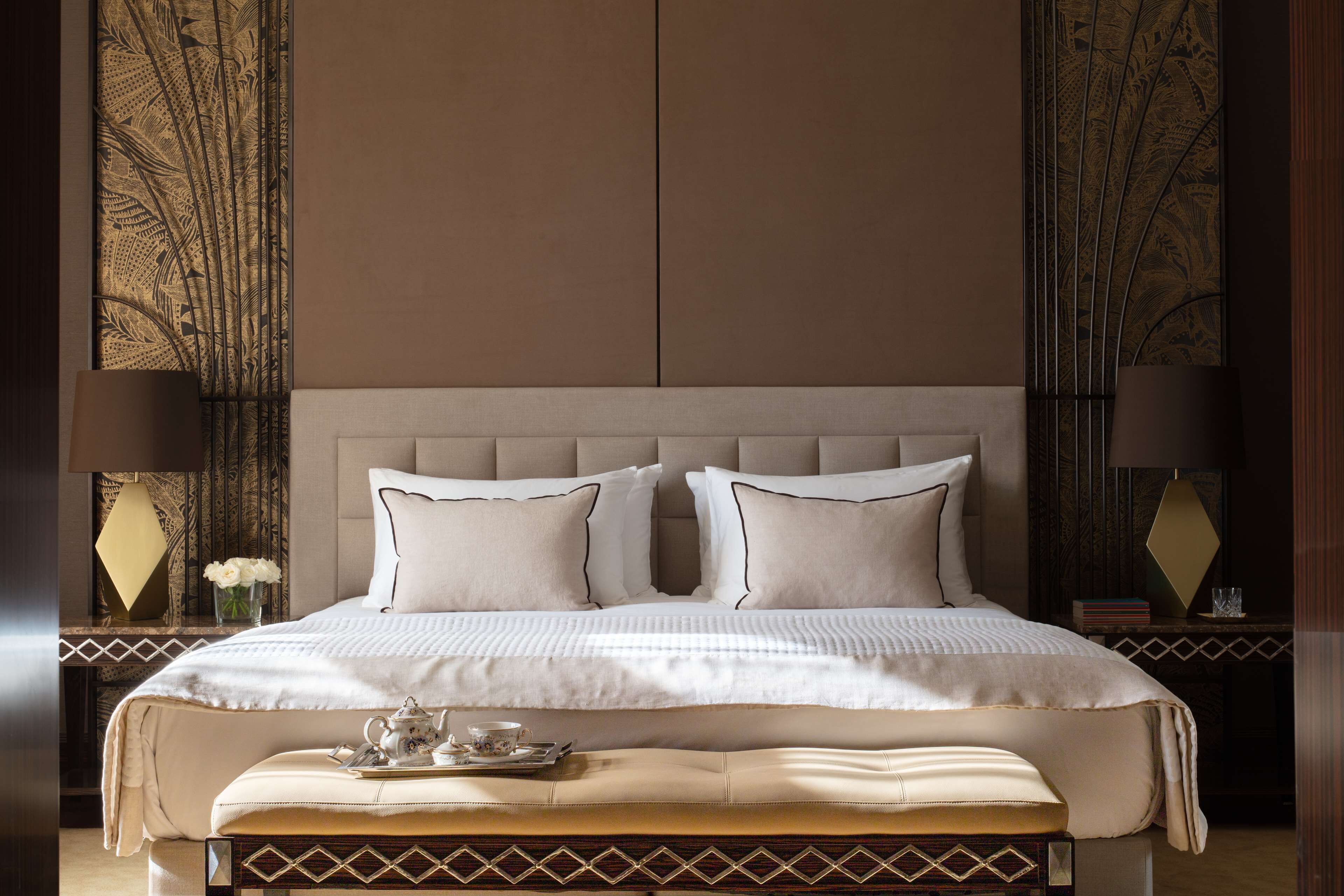 A large bed with a headboard, two bedside tables with lamps, and a decorative wall panel.