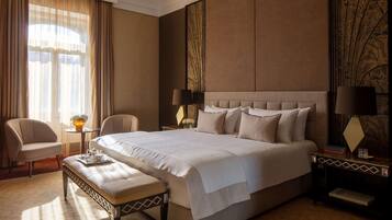Ruime hotelkamer met een groot bed, een zithoek met een bank, twee stoelen, een bijzettafeltje en een decoratief paneel.