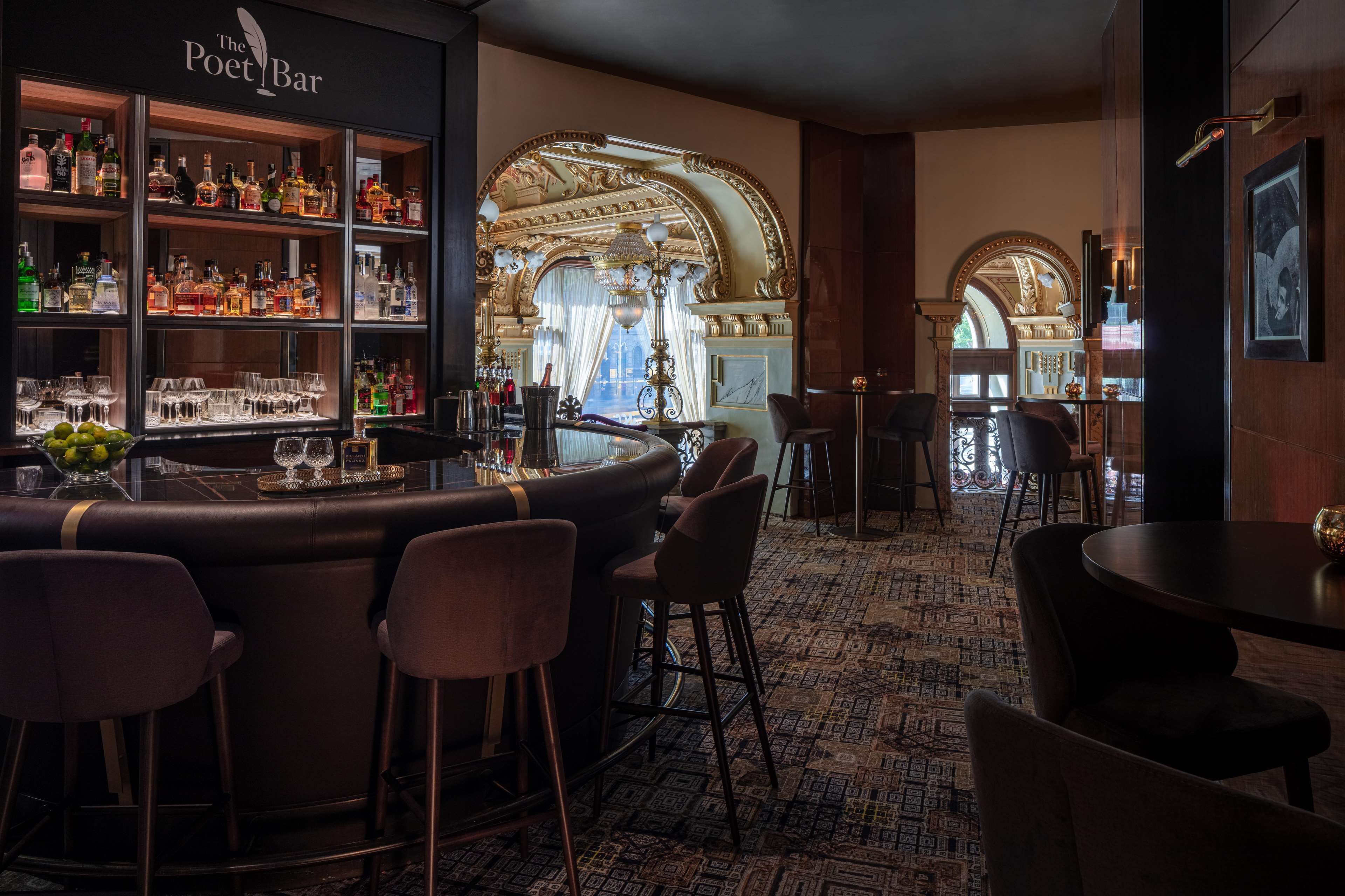 A bar area with a bar counter, stools, and shelves of bottles.