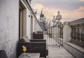 A balcony with wicker furniture, a glass of drink, and a magazine.