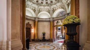 A grand lobby with a marble floor, ornate columns, a large floral arrangement, and a stained glass ceiling.