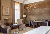 A hotel room with a bed, two chairs, a desk, a lamp, and a wall with a bird mural.