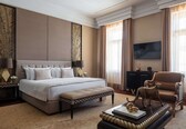 A spacious bedroom with a large bed, a bench, a sofa, and a television on the wall.