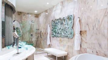 A modern bathroom with a marble wall, a glass shower enclosure, a white bench, and a bathtub.