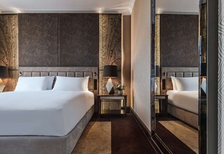A modern hotel room with a large bed, a nightstand, a mirror, and decorative wall panels.