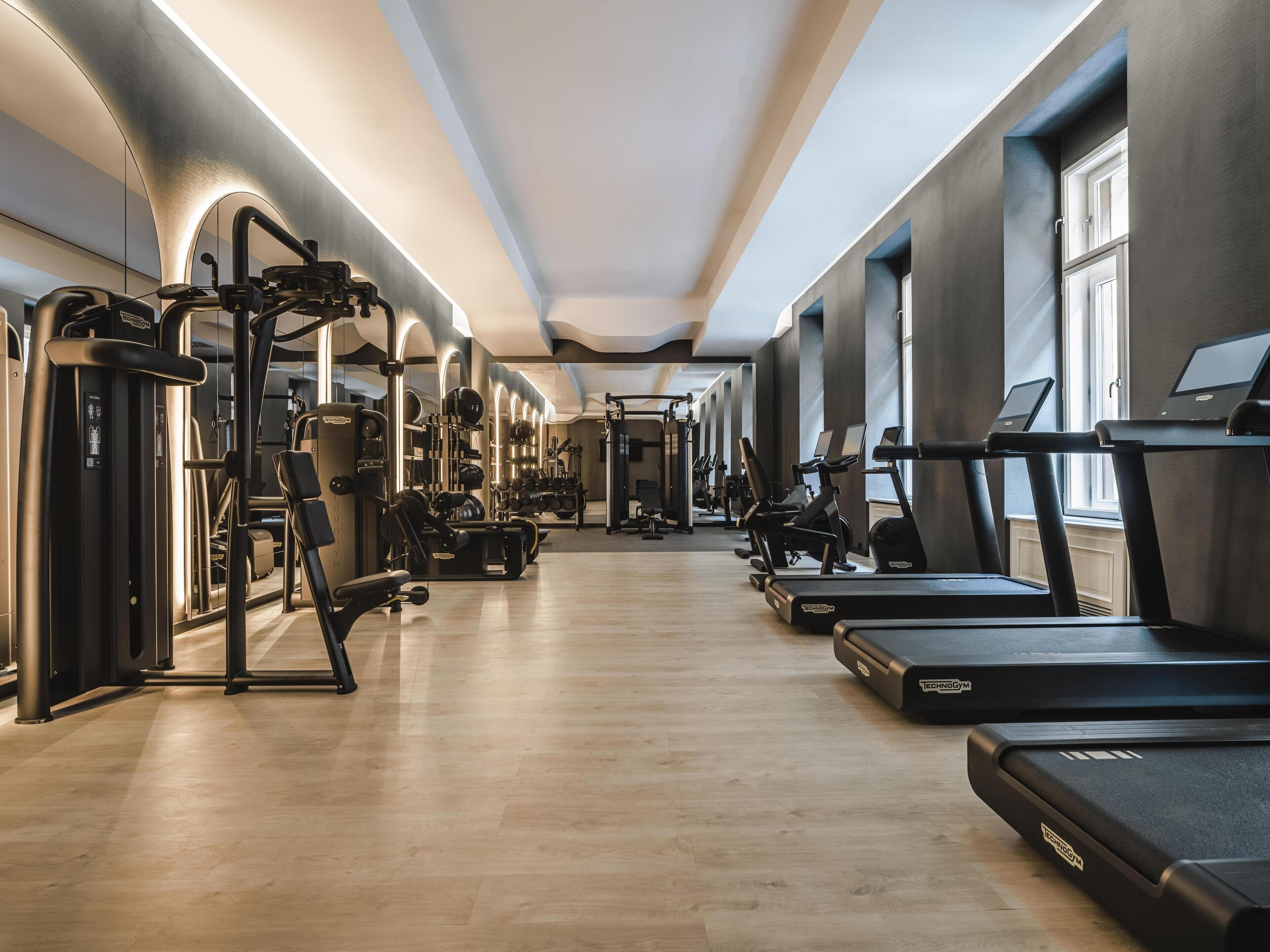 Uma academia moderna com diversos equipamentos de exercício, incluindo esteiras e aparelhos de musculação, dispostos em um espaço amplo com grandes janelas que oferecem luz natural.
