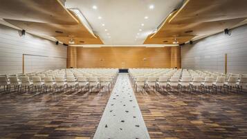 Un salón de conferencias con filas de sillas, un pasillo central y suelo de madera.