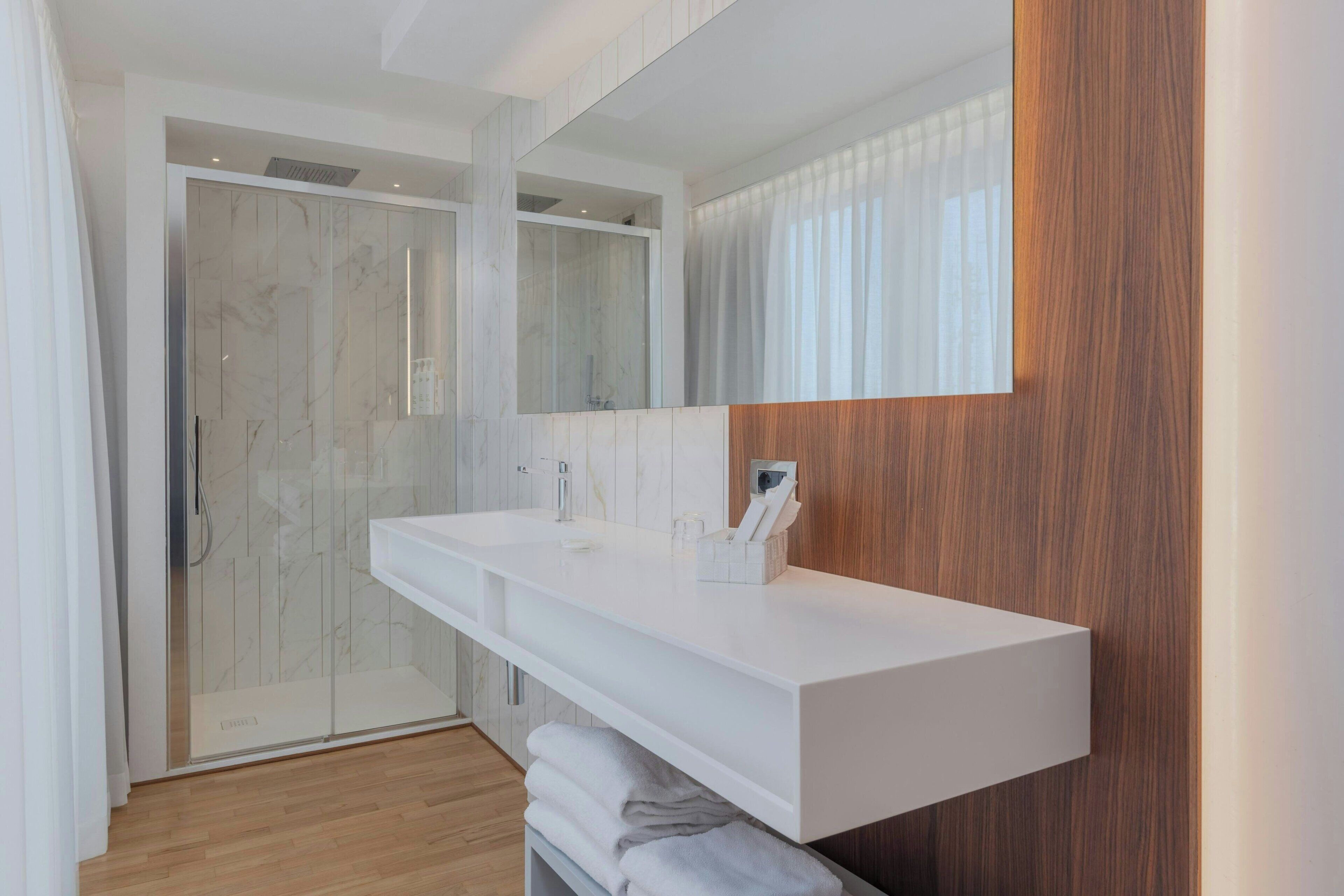 Un baño moderno con un tocador blanco, un espejo grande y una pared de acento de madera.