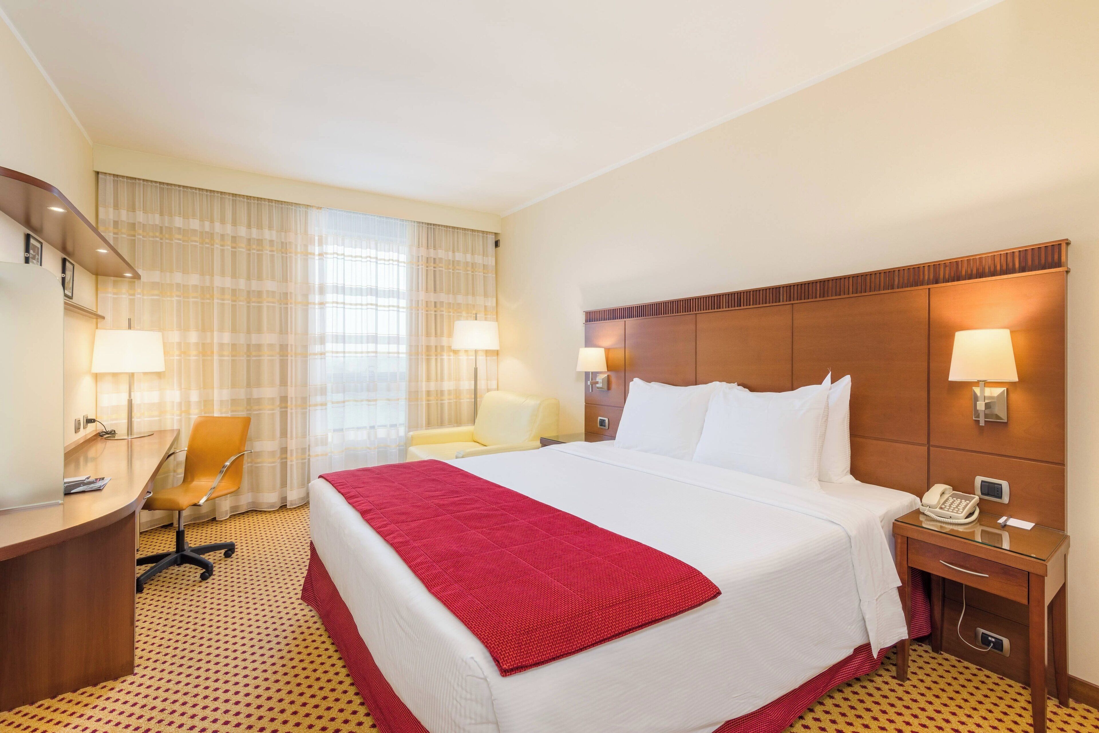 Ein Hotelzimmer mit einem großen Bett, einem Schreibtisch, einem Sessel und zwei Nachttischlampen.